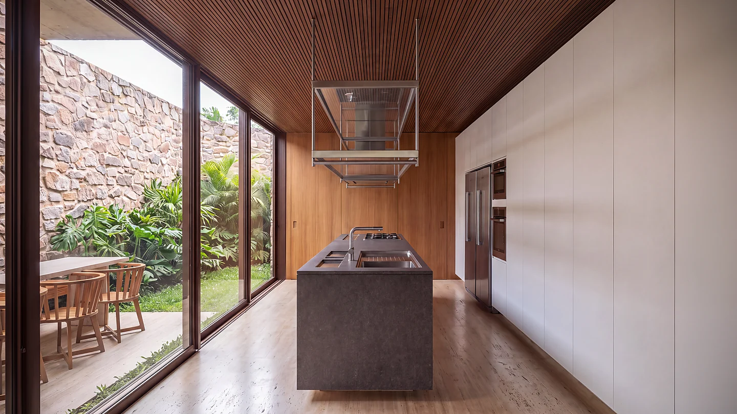 Cozinha da Casa Maré com ilha em pedra e abertura para jardim interno