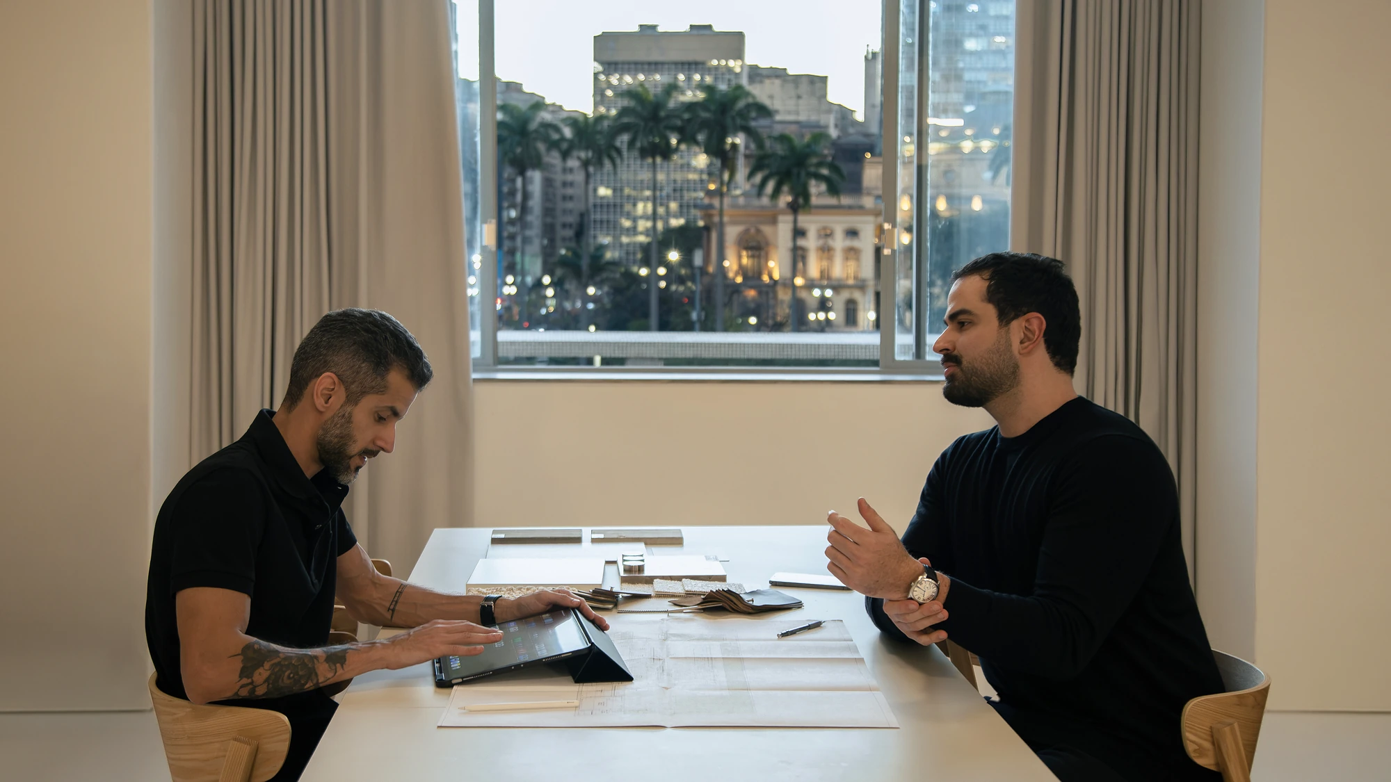 Adonis Penalva e João Felder em reunião no escritório do Studio Maio, com a cidade de São Paulo ao fundo